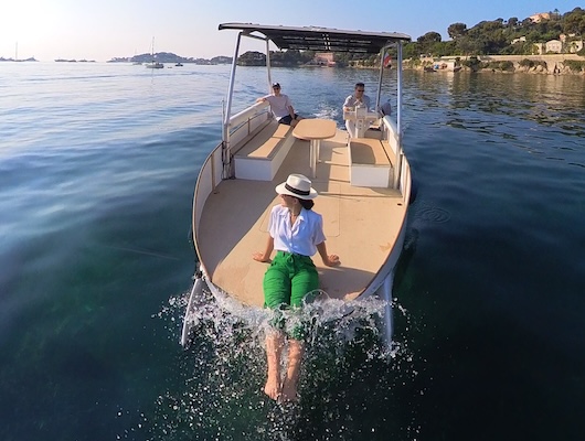 Person relaxing on front of boat, trailing hands in water, with two others seated behind.