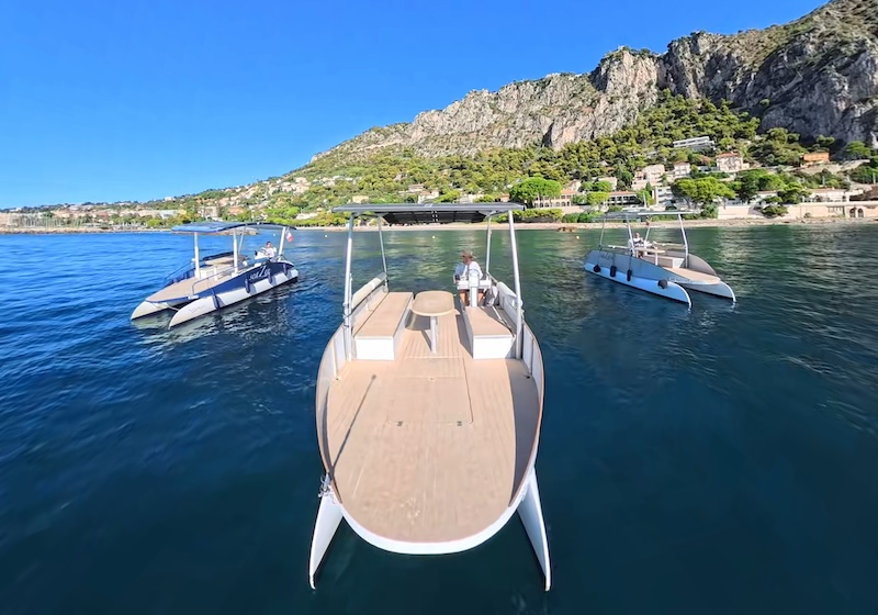 Three wooden boats on a clear blue sea near rocky coastline and houses.