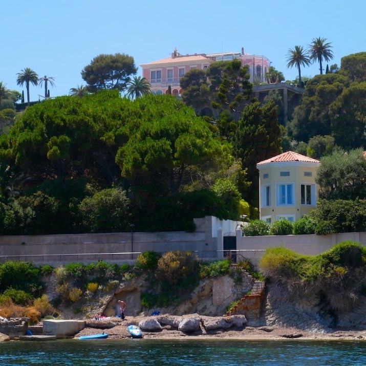Beachfront house with trees and distant hillside villa.