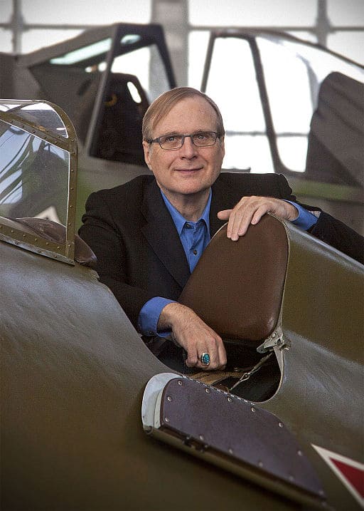 Person in a blue shirt and black jacket seated in a vintage airplane cockpit.