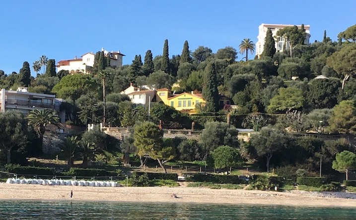 Houses on a hillside with trees, overlooking a beach and ocean.