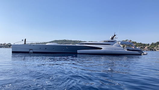 A sleek, modern yacht on calm blue water with a distant hilly coastline.
