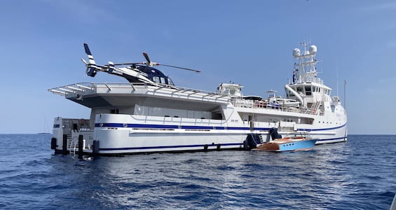 Large yacht with a helicopter on deck and a boat alongside on calm sea.