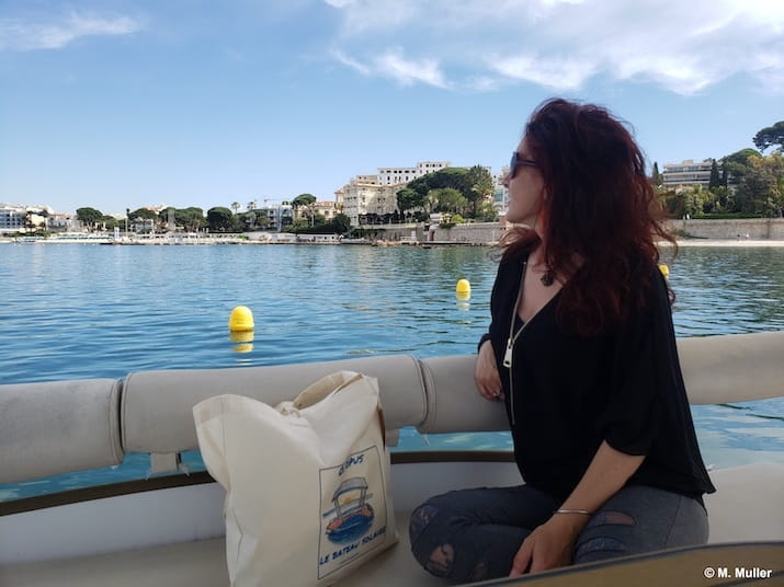 Person on a boat looking at waterfront buildings and buoys in calm water.