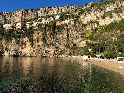Coastal cliffside with houses, clear water, and a small sandy beach.