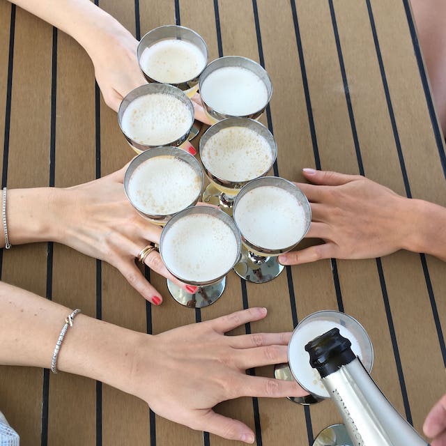 Four hands clinking six glasses of champagne over a wooden table.