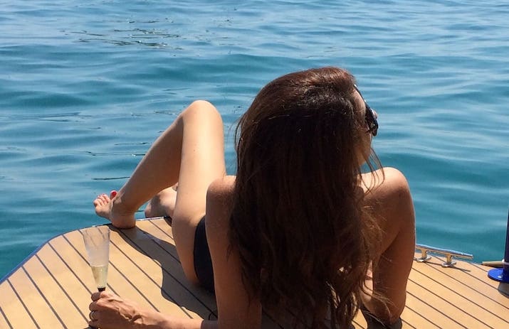 Woman with long hair sunbathing on a boat with glass in hand.