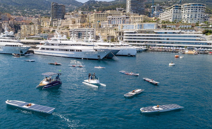 Multiple solar-powered boats in a harbor with yachts and cityscape background.