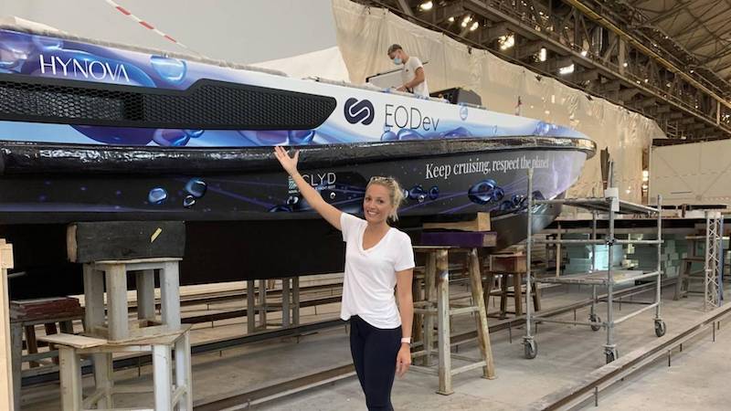 Person standing next to large boat in a workshop setting.