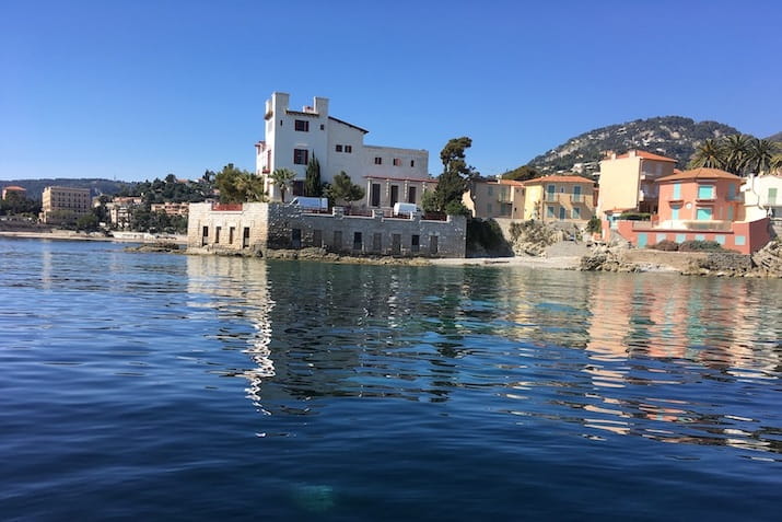 Coastal houses by calm sea with mountains in background.