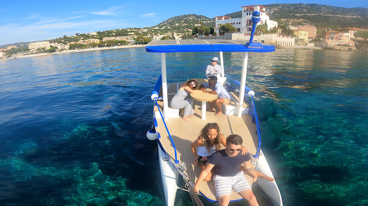 Group of people relaxing on a boat in clear blue water near a coastal town.