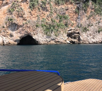 Boat deck view of rocky cliff with cave opening and ocean water.