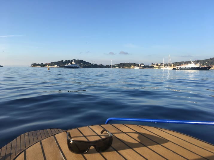 Sunglasses on a boat deck overlooking a calm sea with yachts in the distance.