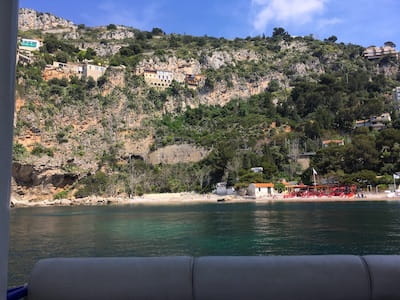 Rocky hillside with houses above a small beach by calm water.