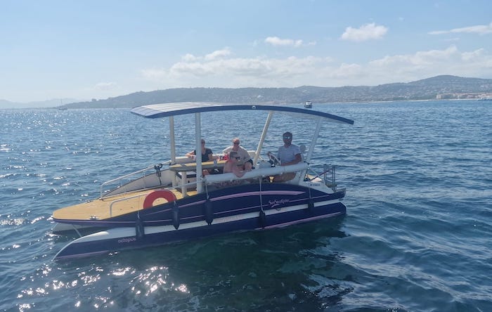 Three people on a small boat with a canopy on a sunny day at sea.