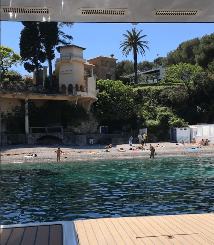 View of beach and buildings from a boat, with trees and a clear blue sky.