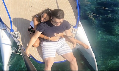 Couple sitting on a boat's edge, hugging near clear blue water.