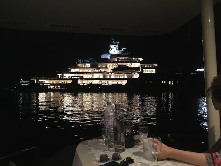 Night view of a lit-up yacht from a nearby boat with a table on deck.