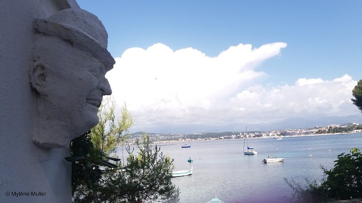 Stone face sculpture overlooking a bay with boats and distant shoreline.