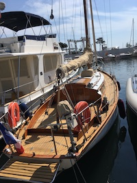 Wooden sailboat docked beside larger boat in marina.