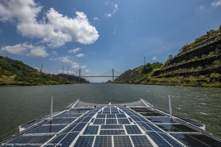Solar-powered boat cruising under a bridge on a river.