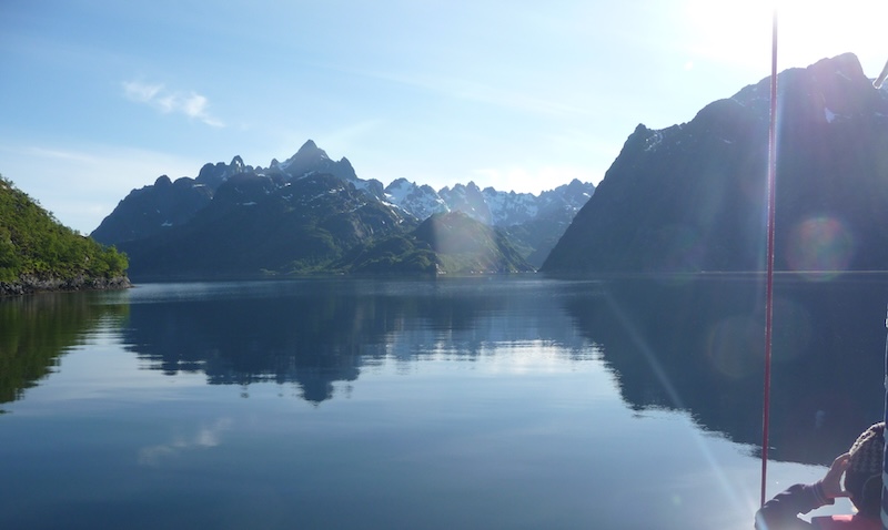 Calm water reflecting mountains under a clear blue sky.