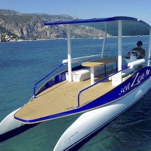 Modern catamaran with deck cover on calm water near mountains.