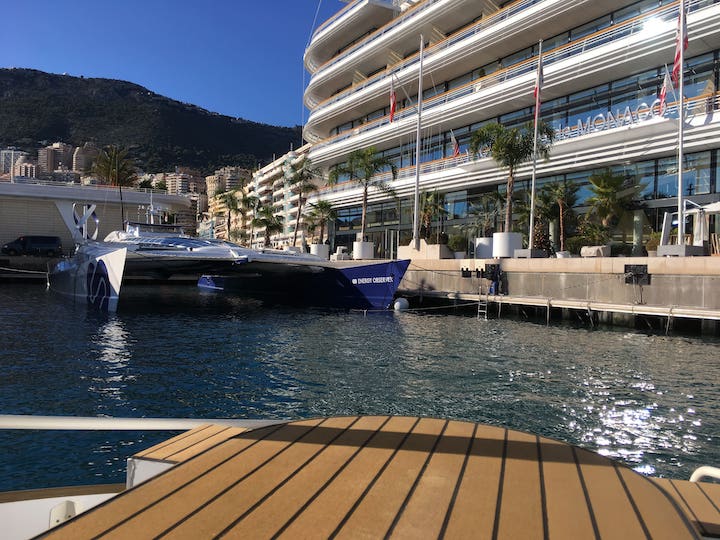 Docked futuristic yacht beside modern building in sunny harbor.
