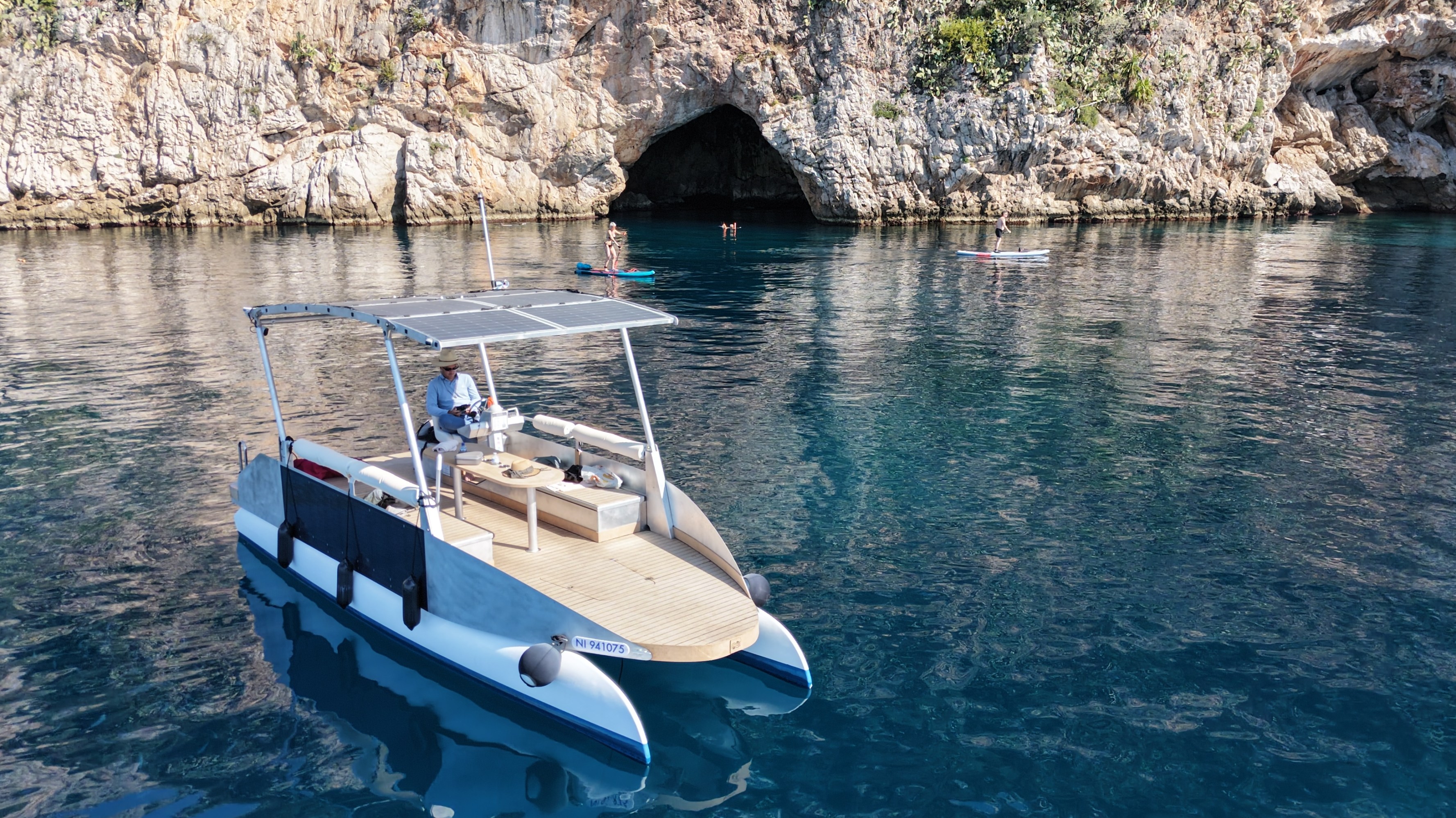 Small boat near a rocky cave with people swimming, clear water