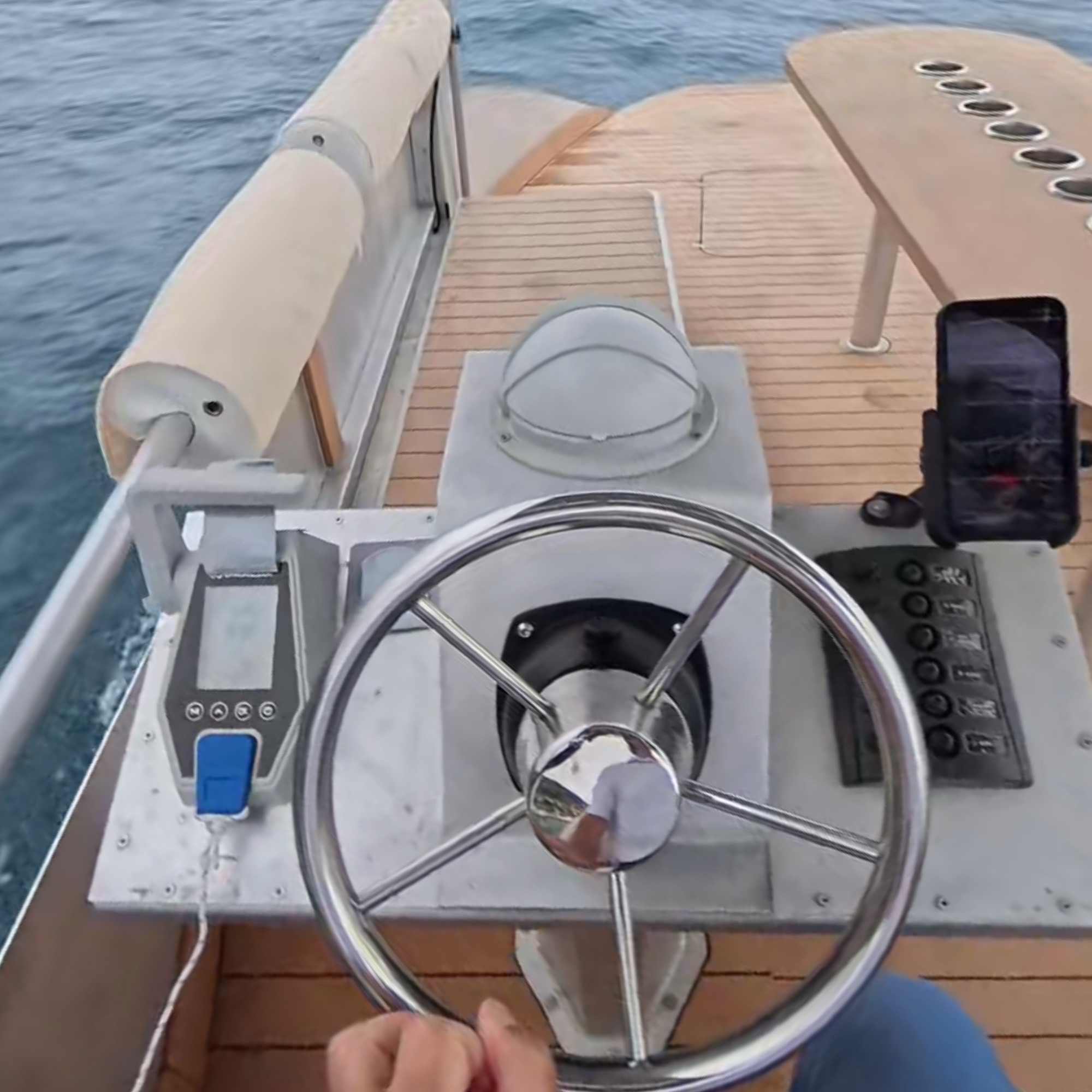 Person steering a boat with a smartphone mounted on the dashboard.
