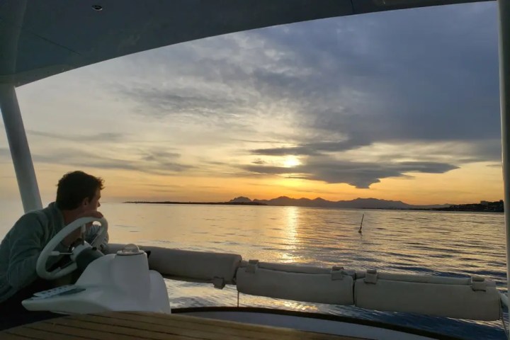 Person steering a boat on calm water at sunset.
