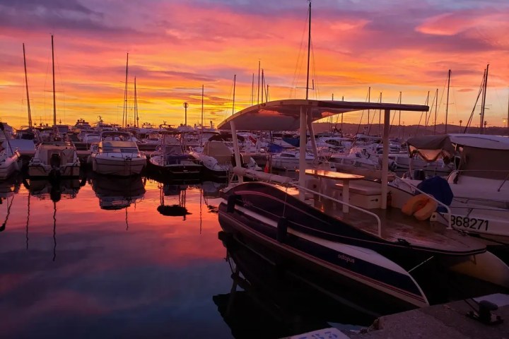Colorful sunset over a marina with boats reflecting on calm water.