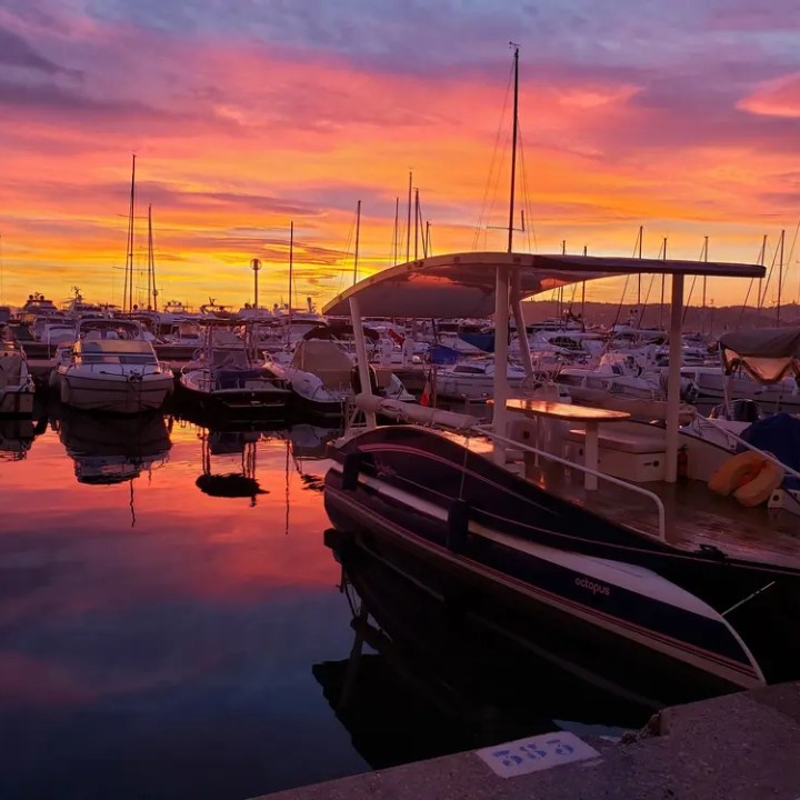 Colorful sunset over a marina with boats reflecting on calm water.
