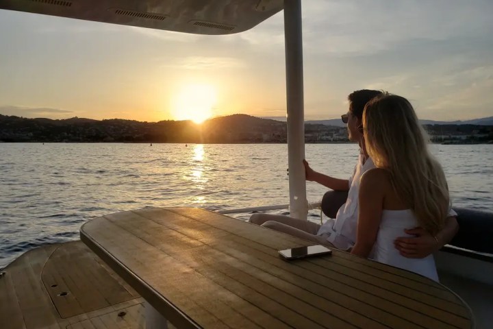 Couple sitting on a boat, hugging, watching a sunset over the water.