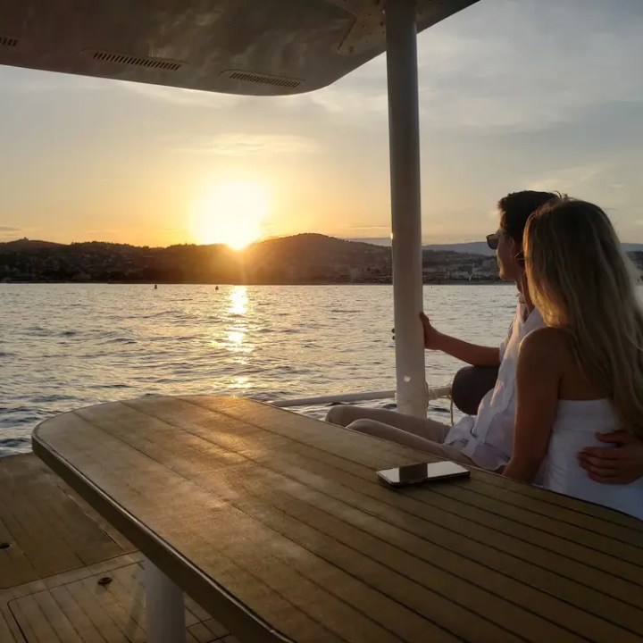 Couple sitting on a boat, hugging, watching a sunset over the water.
