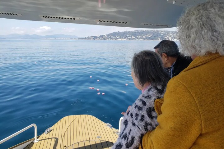 Three people on a boat deck view floating flowers on a serene blue sea.