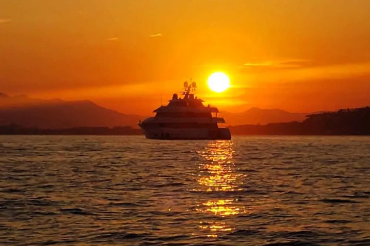 Yacht on the water at sunset with orange sky and sun reflection.