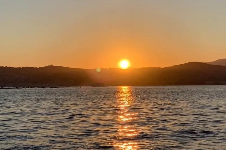 Sunset over a calm sea with hills visible in the background.