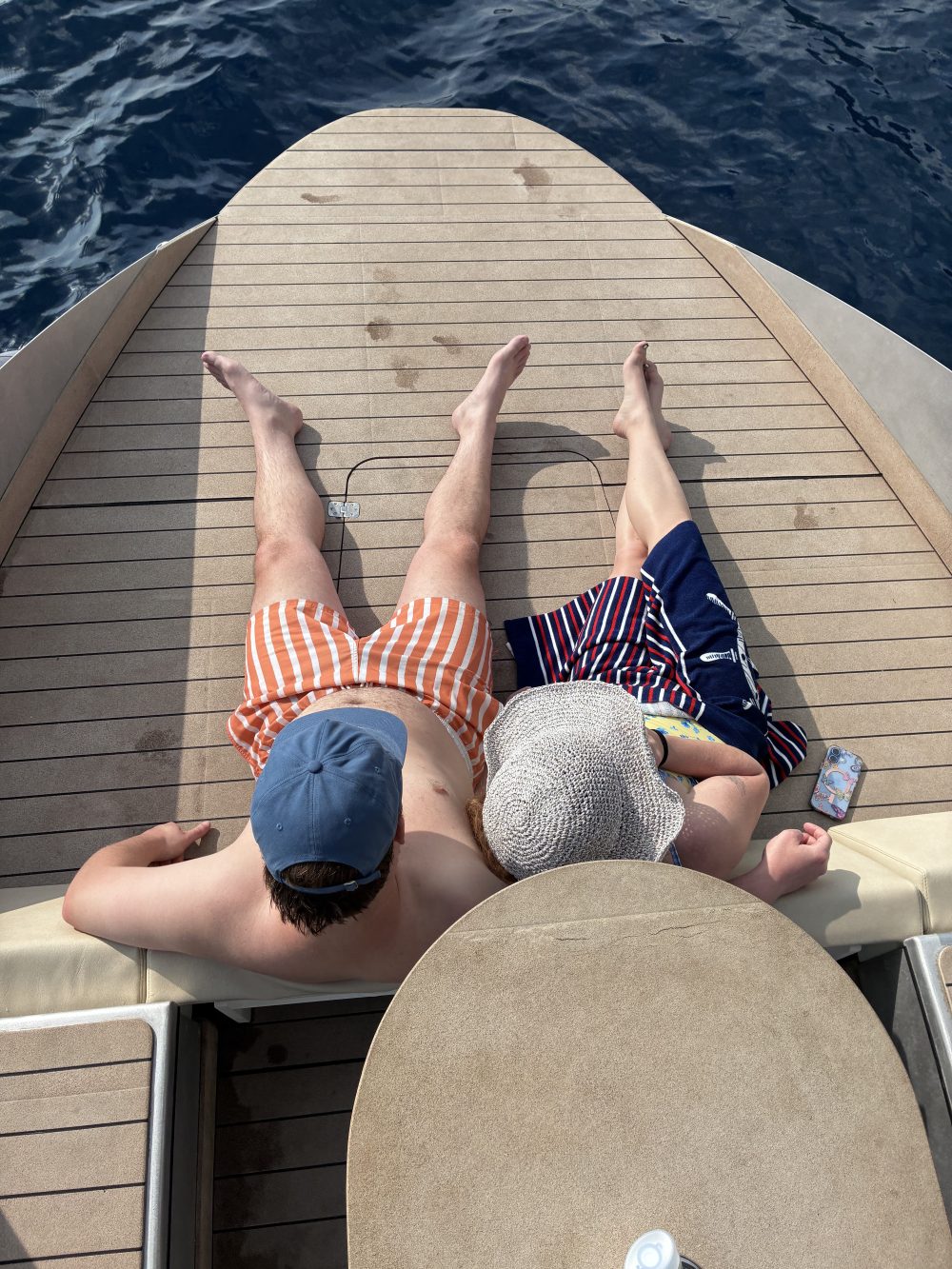 Two people relaxing on a boat deck near the water.