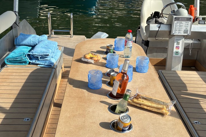 Boat table with drinks, snacks, towels, and sunlight on water.