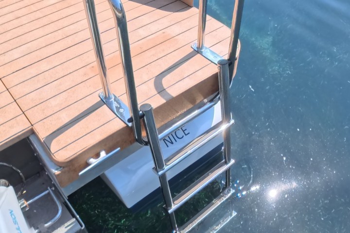 Boat stern with wooden deck and metal ladder in clear water.