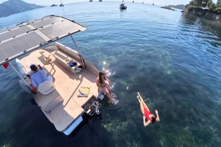 People on a boat in clear water; one person swimming nearby.