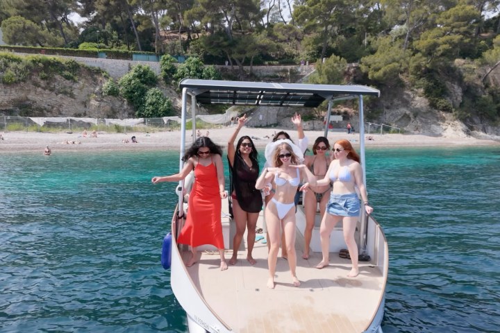 Six people on a boat, enjoying sunny weather near a beach.