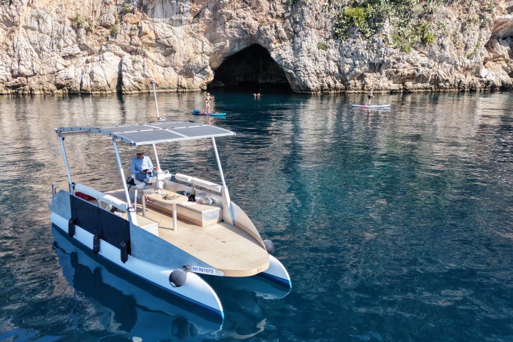 Catamaran docked near a rocky cave, with clear blue water and swimmers nearby.