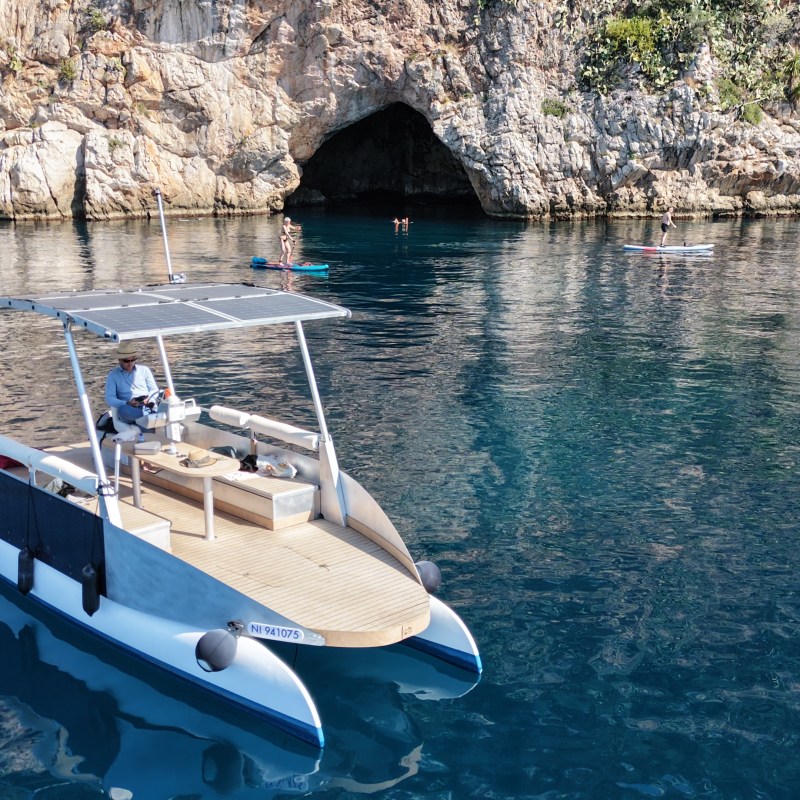 Catamaran docked near a rocky cave, with clear blue water and swimmers nearby.