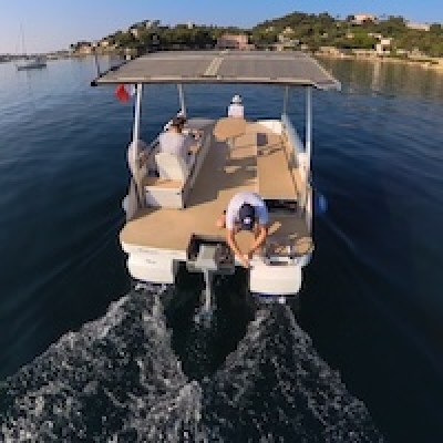 Small motorboat with solar roof on calm water, two people on board.