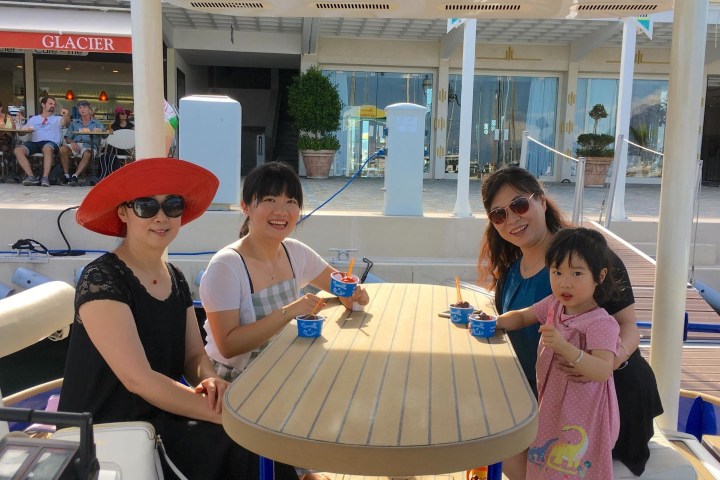Four people at a table on a dock, eating ice cream near a café. One woman wears a red hat.