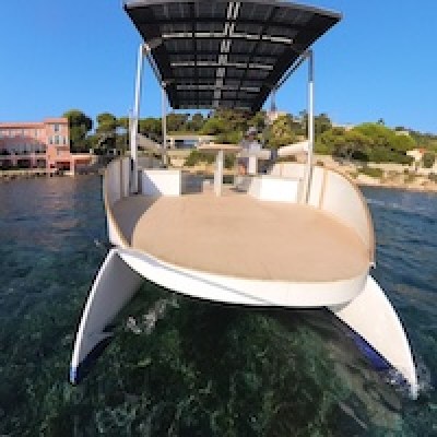 Eco-friendly solar-powered boat near a coastline with clear water and buildings.