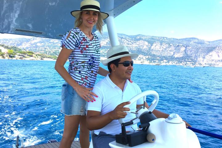 Smiling man and woman in hats on a boat in ocean with scenic mountains in background.