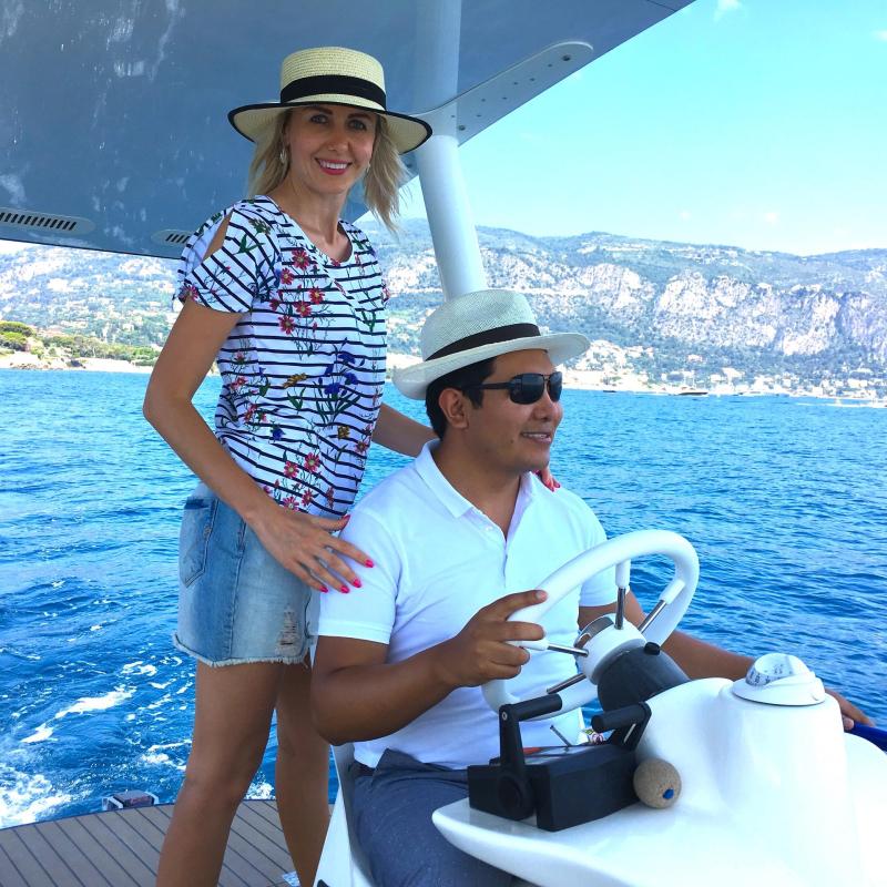 Smiling man and woman in hats on a boat in ocean with scenic mountains in background.